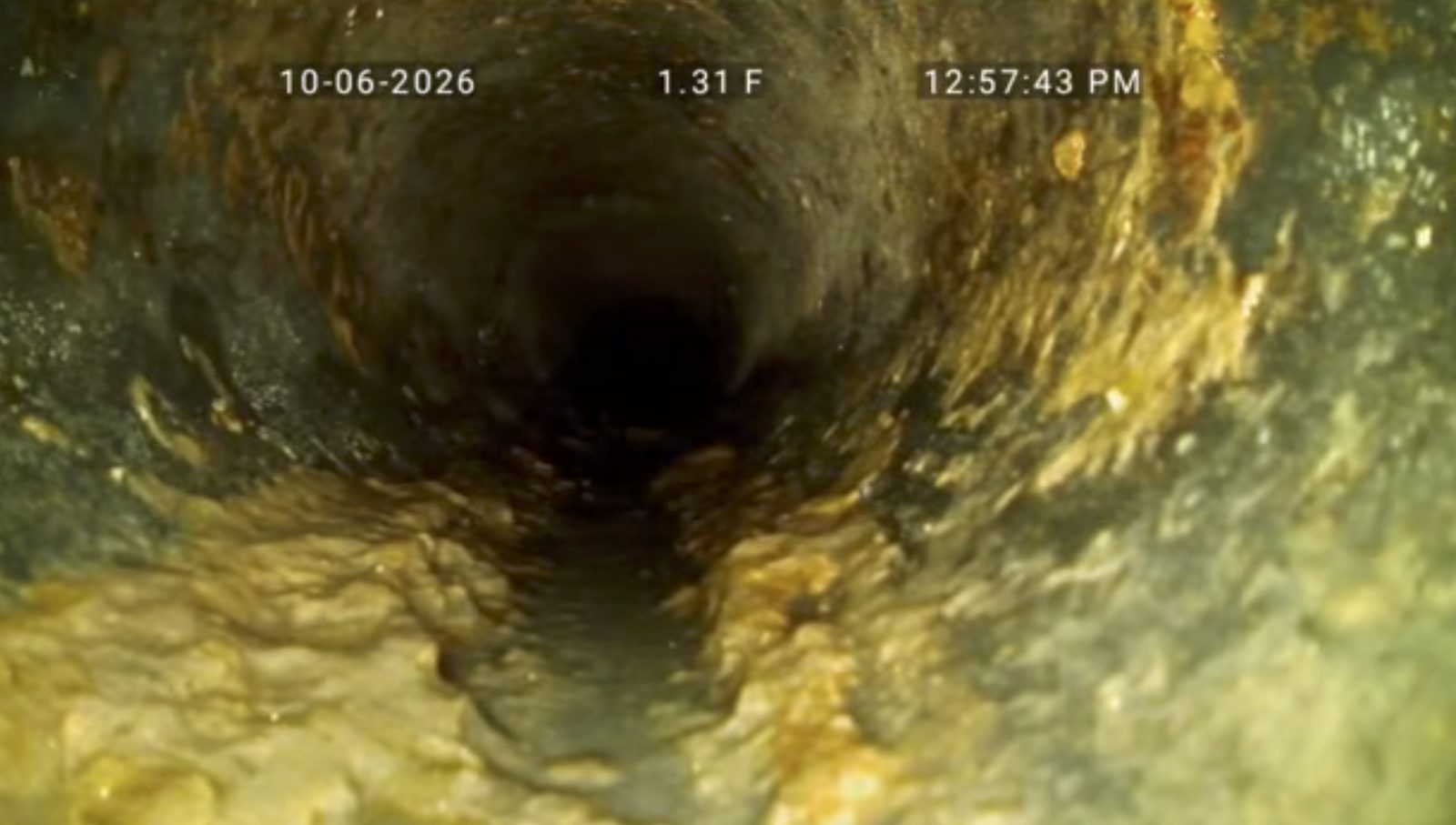 Heavy grease buildup along the bottom of a sewer pipe beneath a kitchen sink
