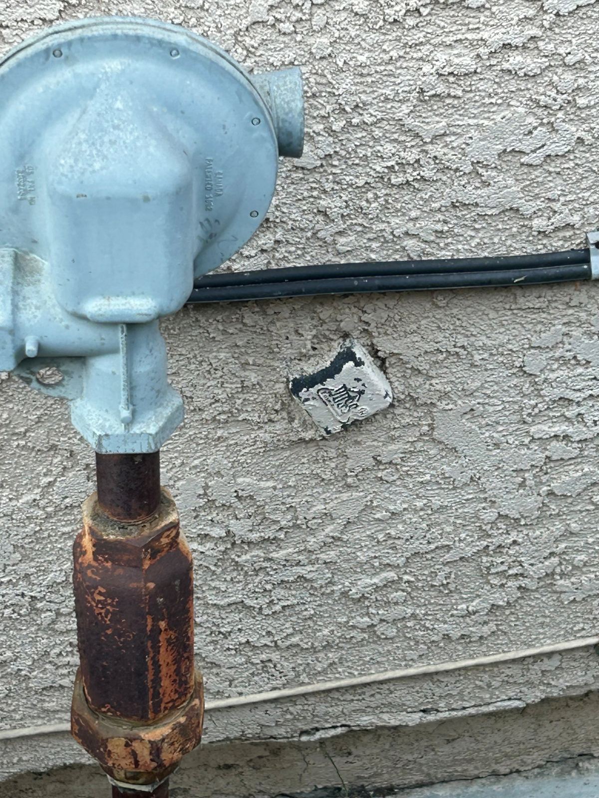 Sewer cleanout plug stuccoed over on a house wall, with only the square nut showing