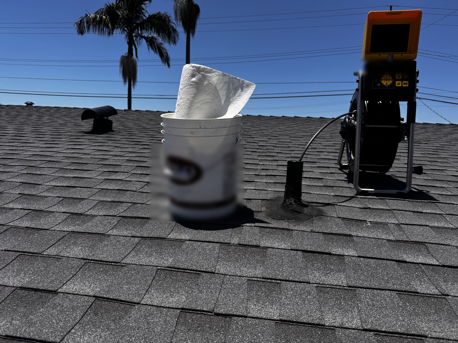 Sewer inspection camera reel and monitor staged on a composition shingle roof beside an open plumbing vent stack