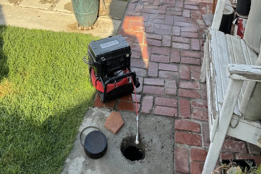 Sewer scope camera and reel deployed at a ground-level cleanout beside a brick walkway